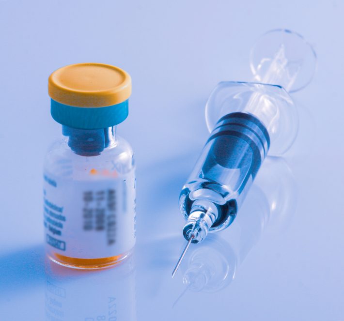 Closeup shot of a syringe and a vial on a glossy surface